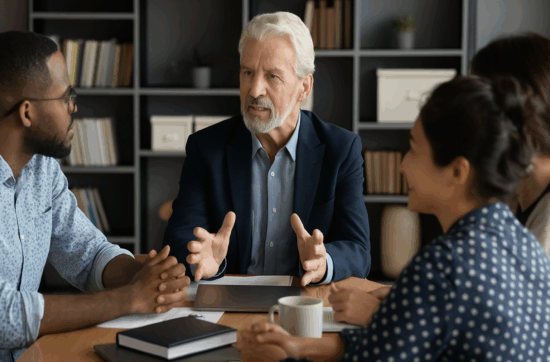 Quatre professionnels discutant autour d’un ordinateur dans un environnement moderne et collaboratif, représentant un cadre favorable à la formation continue en entreprise.